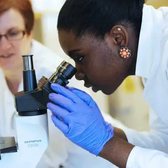 female student looking into a microscope in a laboratory