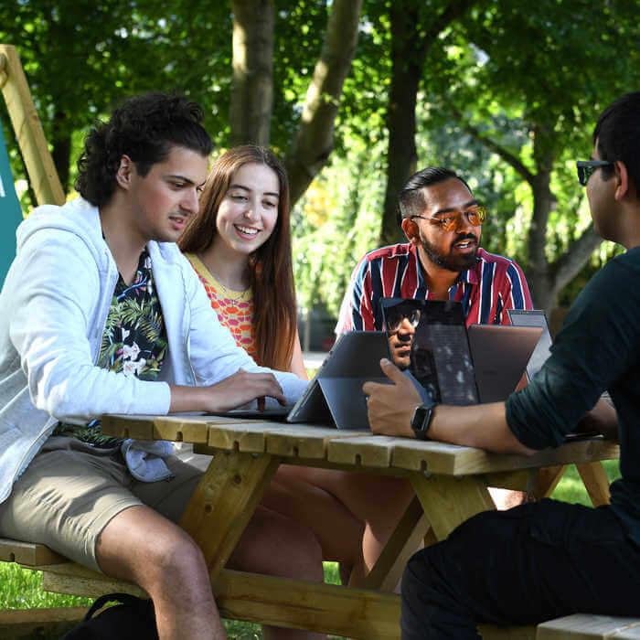 group of students with laptops around a table in a park