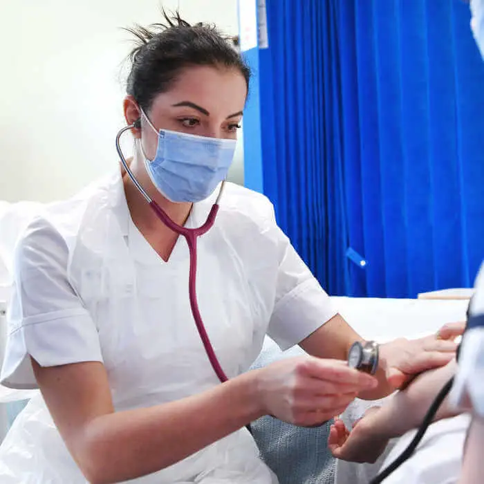 female nurse student wearing a facemask taking patients blood preassure