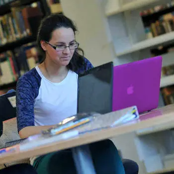 young female student working on a laptop in the library of Brunel University London