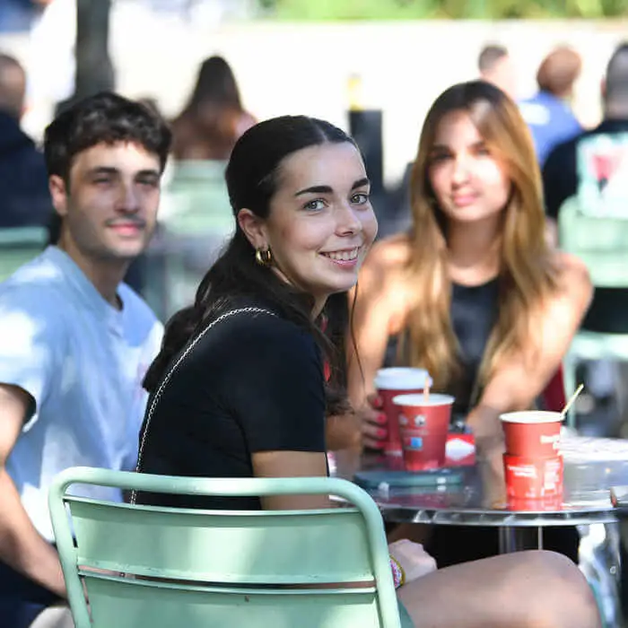 three students drinking coffee around a table outdoors