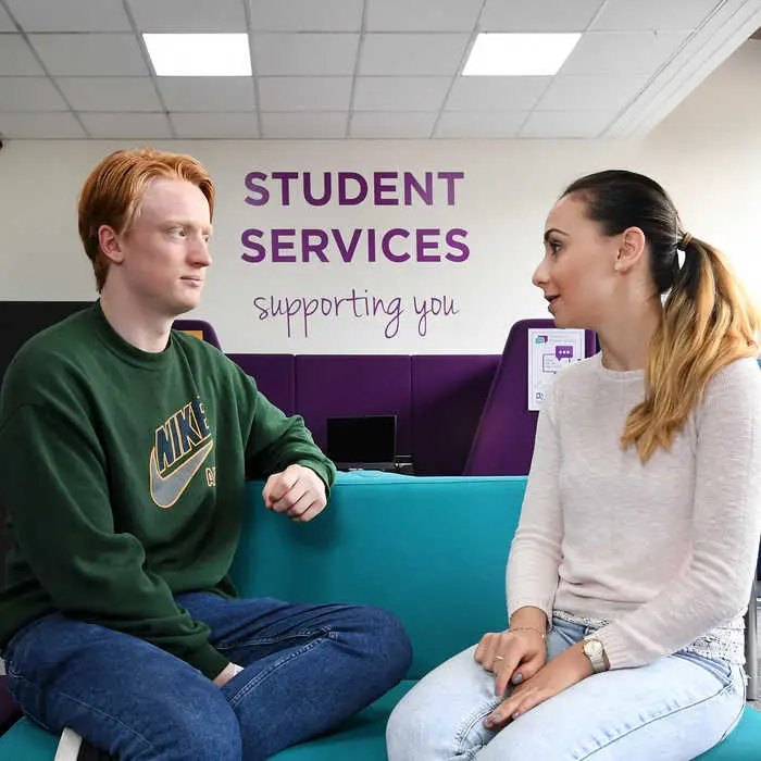 two people chatting with a student services sign on the wall in the background