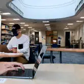 two students in face masks working on their laptops in the university library