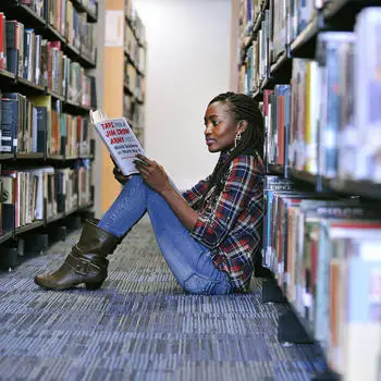 female student reading a book and sitting on the floow in the university library