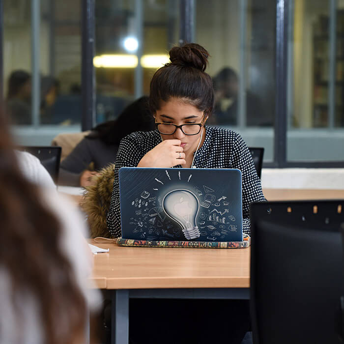 female student reading notes on her laptop in the university library