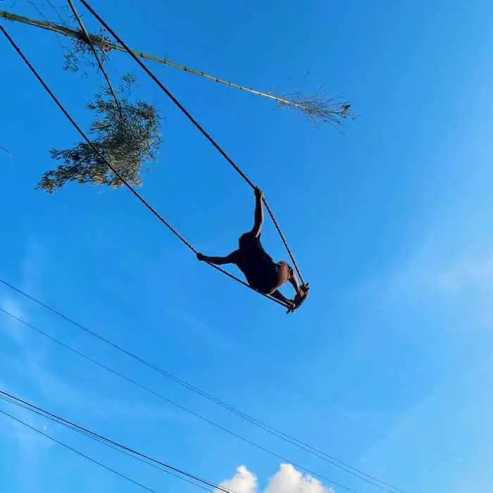 Someone standing on a swing swinging with a blue sky background