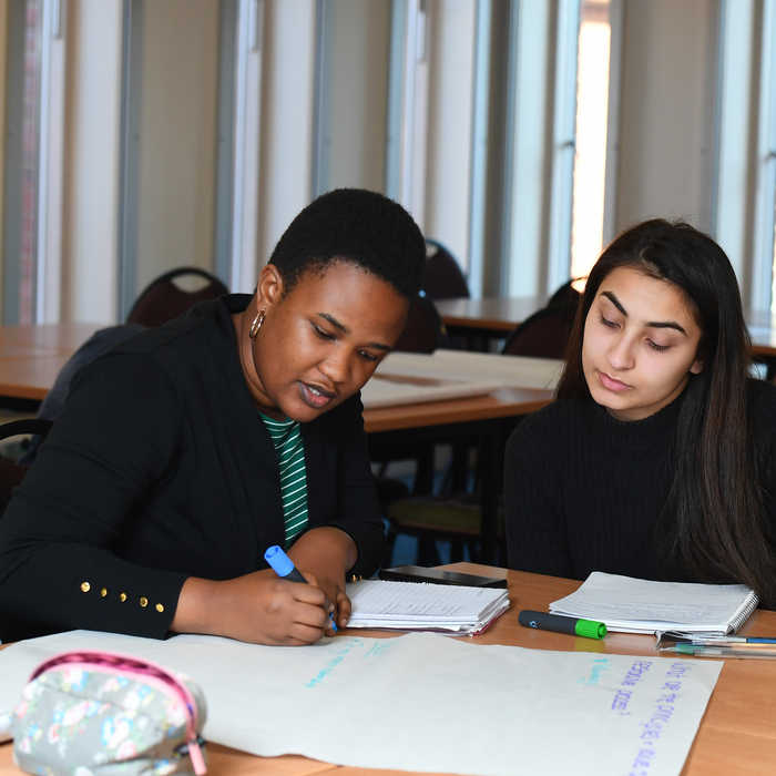 Two female students sitting at a desk and using markers to write on A3 paper