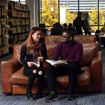 Two students reading book on a brown leather sofa in a library