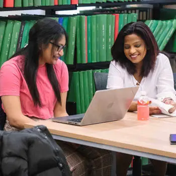 two students talking and looking at a lap top