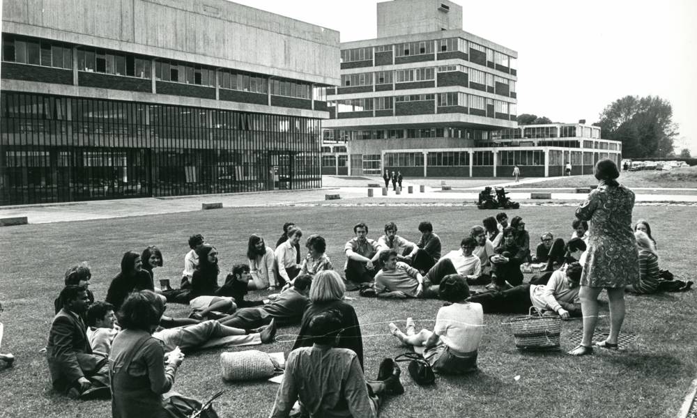 Black and white image of students sitting on grass in front of buildings