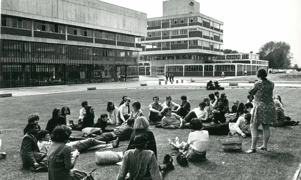 Black and white image of students sitting on grass in front of buildings