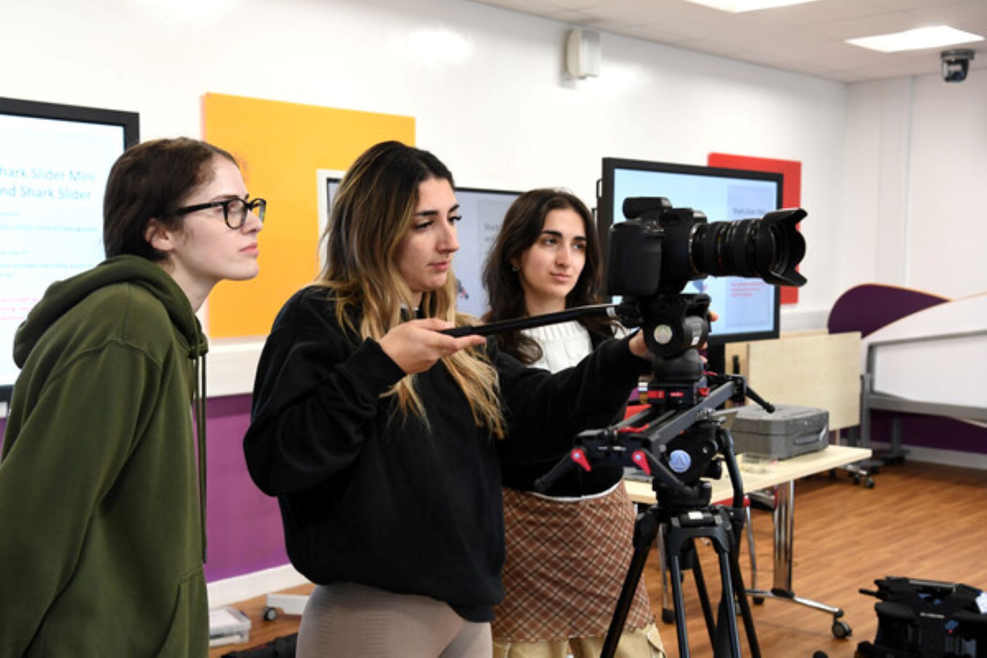 female film students standing and using a camera in a classroom