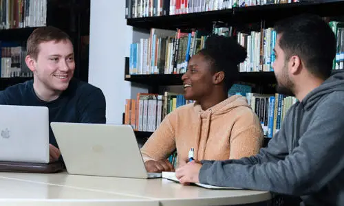 Three people engaged in a discussion with laptops