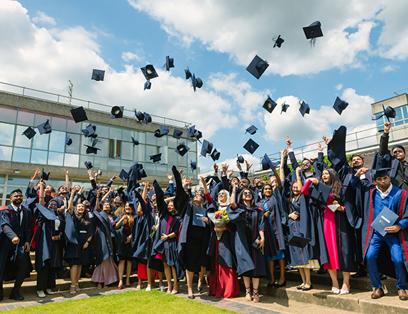 Group of graduates in caps and gowns joyfully throwing their hats in the air outdoors