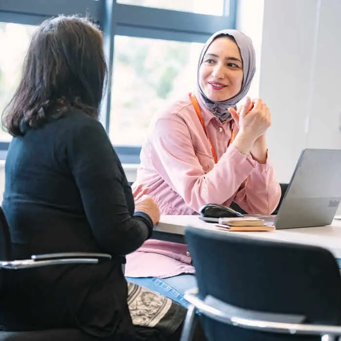 Two women having a discussion at a table with a laptop and notebook