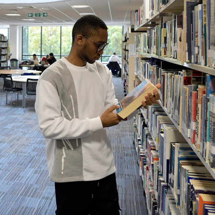 A man wearing glasses browsing books on a library shelf 