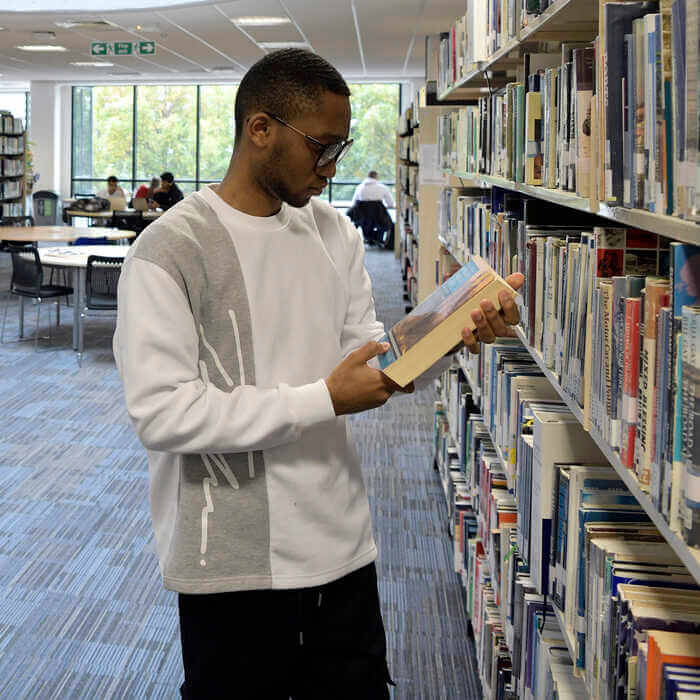 A man wearing glasses browsing books on a library shelf