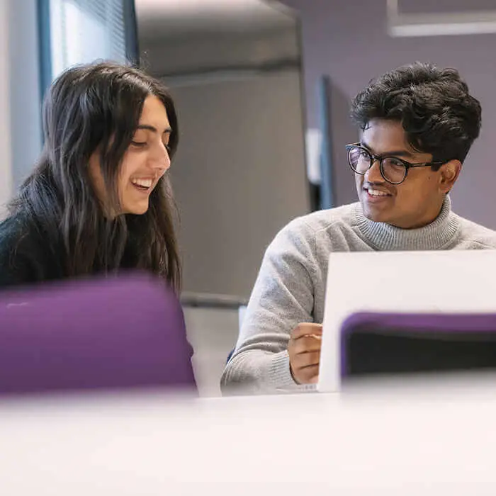 Two students smiling and working together on a laptop