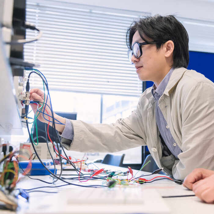 Young man with glasses working on electronic circuits and wires in a bright laboratory or classroom setting