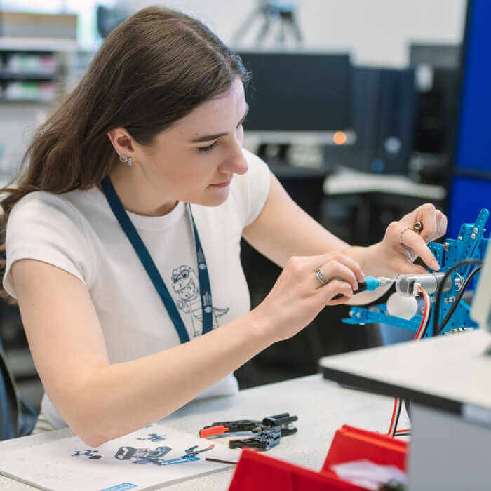 Young woman assembling a blue robotic arm using a screwdriver at a white desk with tools and instruction sheets