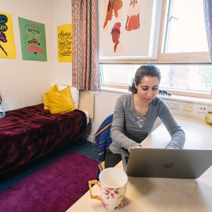 Female student in accommodation sitting at desk and using a laptop