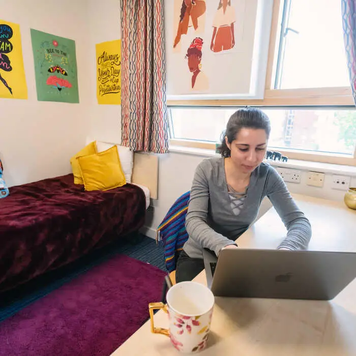 Female student in accommodation sitting at desk and using a laptop