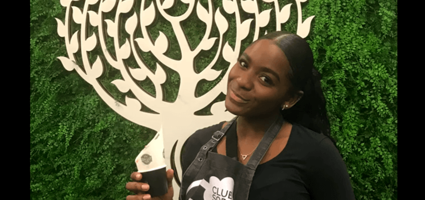 female student smiling and holding a cup with a tree in the background