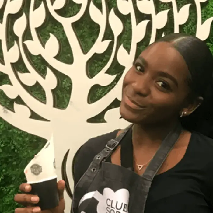 female student smiling and holding a cup with a tree in the background