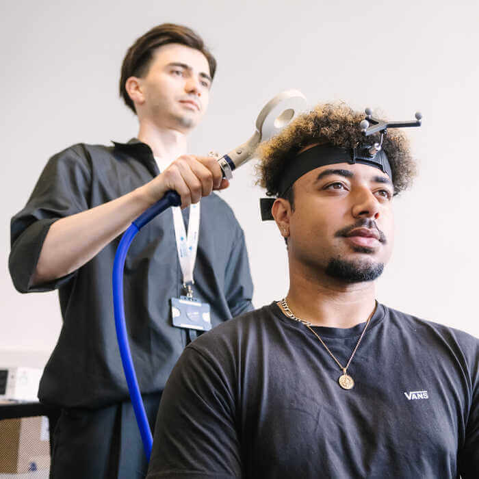 A man wearing a headband with sensors undergoes a brain scan while another man operates the scanning device