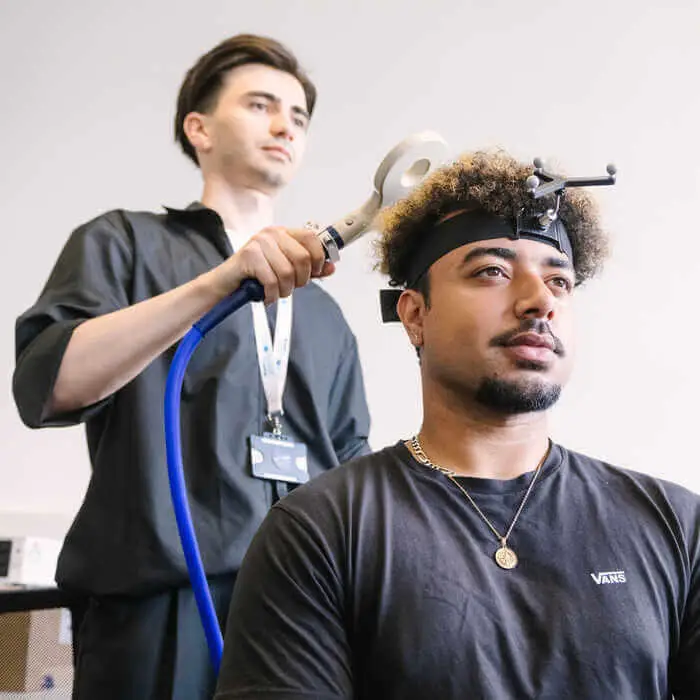 A man wearing a headband with sensors undergoes a brain scan while another man operates the scanning device