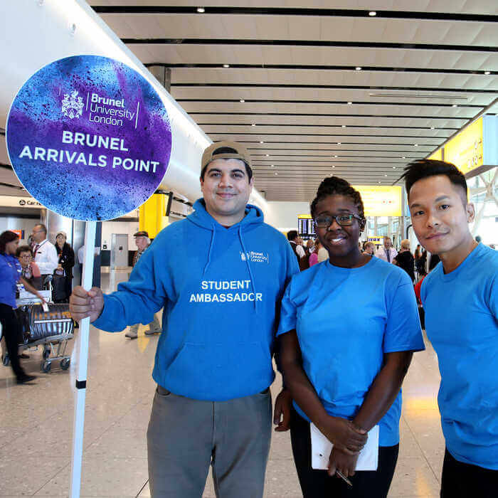 Three Brunel student ambassadors in blue shirts at an arrivals point inside an airport terminal