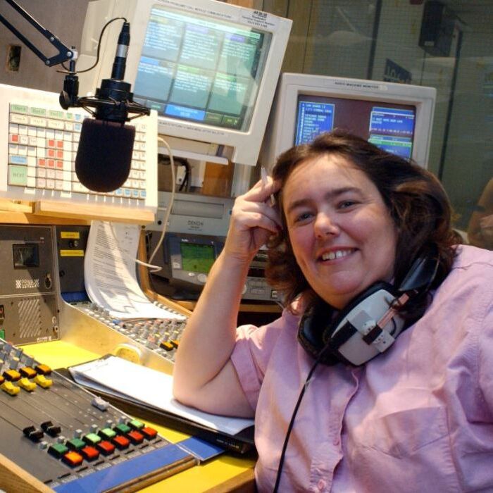 woman sitting on front of computers and sound equipment and microphone and wearing headphones