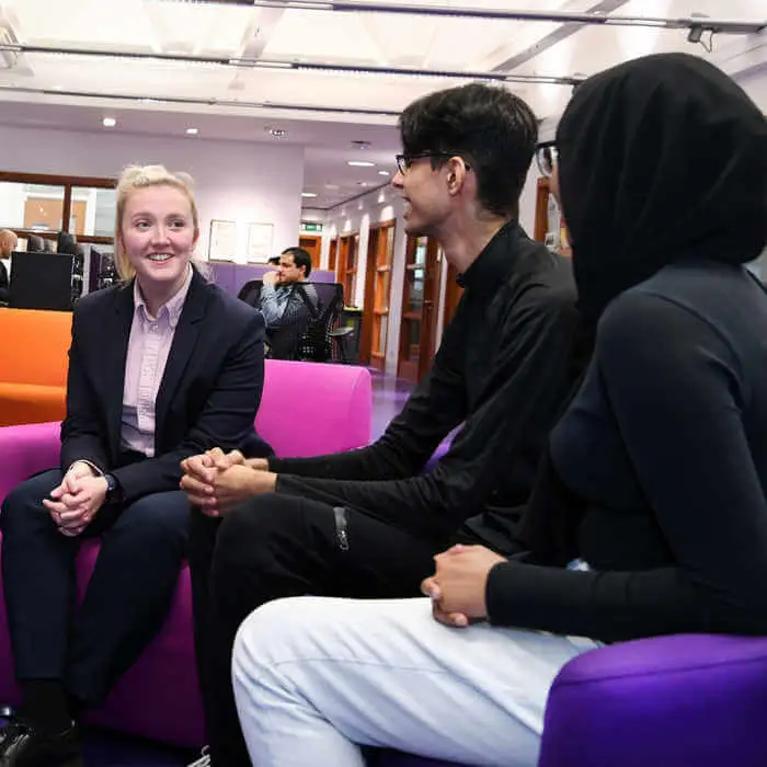 three students sitting on pink and purple sofas talking