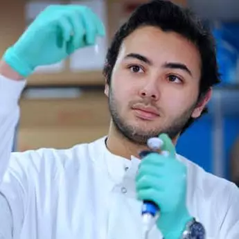 male student in white coat doing experiment in a science lab