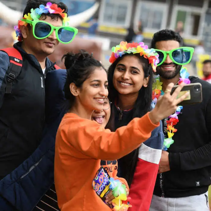 four students taking selfies wearing flower garlands as head pieces