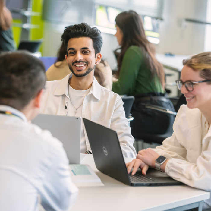 two students with laptops and a lecturer around a table