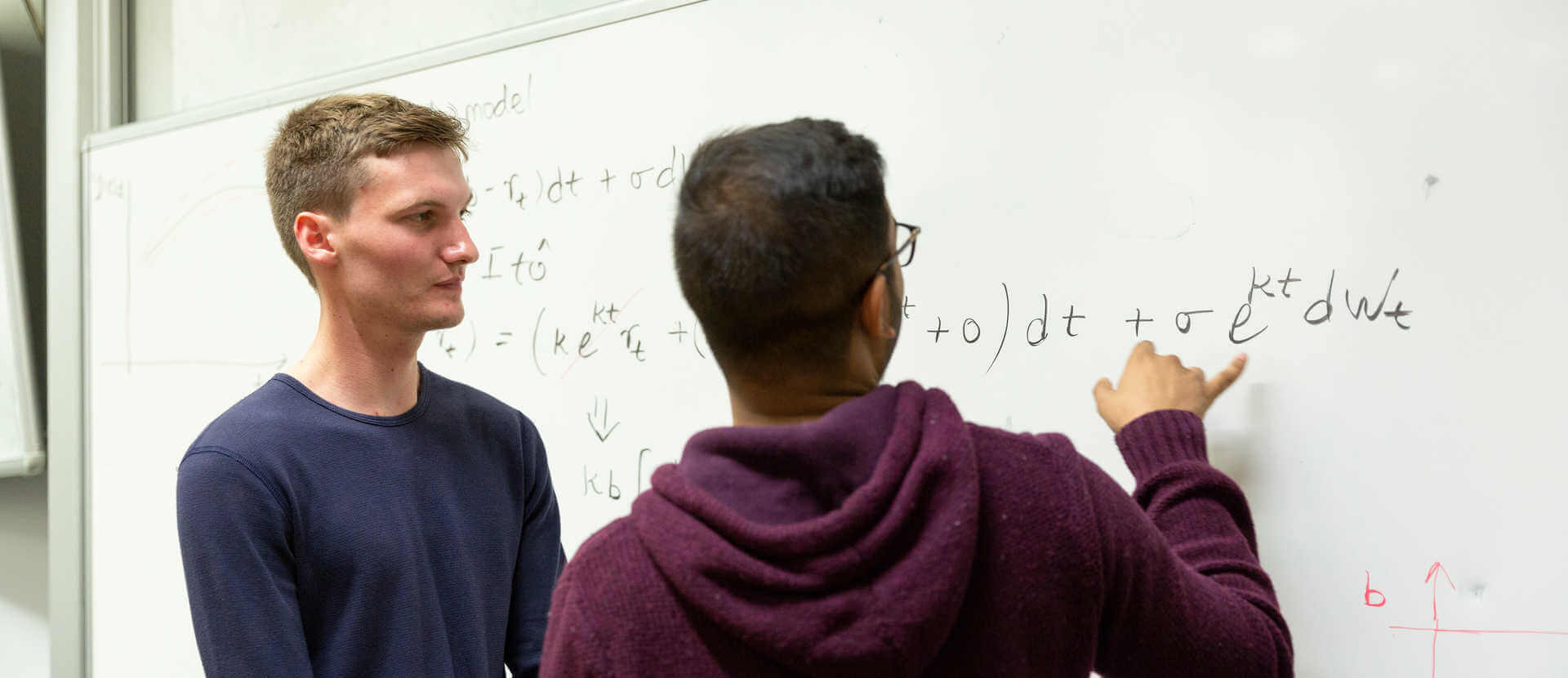 two students solving mathematical problems on a white board