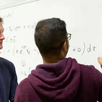 two students solving mathematical problems on a white board