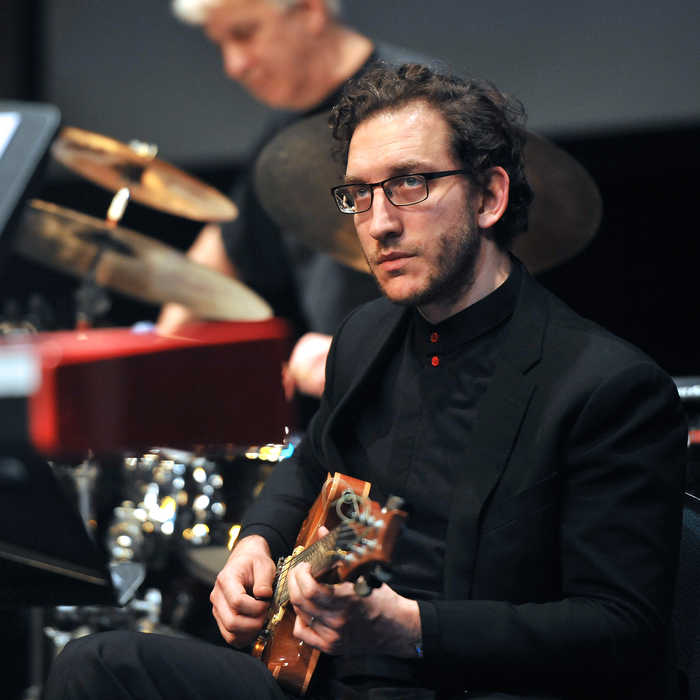 musician playing guitar and another musician playing drums in the background