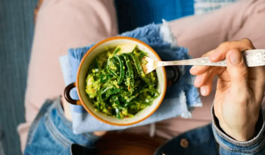 A-person-holds-a-bowl-of-vibrant-green-seaweed-with-a-fork-banner-banner