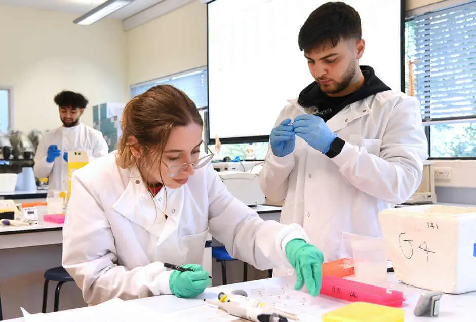 Two students in lab coats work collaboratively in a bright laboratory, focusing on scientific instruments-Banner