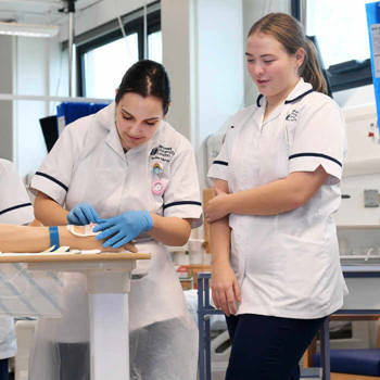 two female nursing students practicing taking blood samples from a manikin arm
