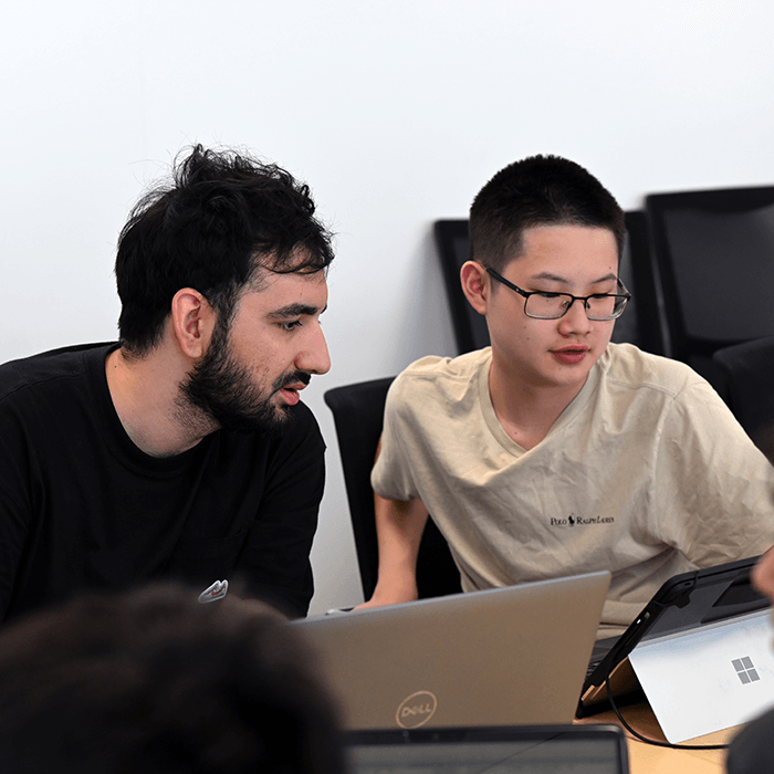 Two individuals engaged in conversation at a table with laptops