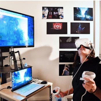Person using VR headset with computer setup and images on the wall.