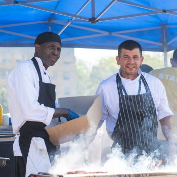 2 chefs cooking outdoors and smoke from the grill on front of them