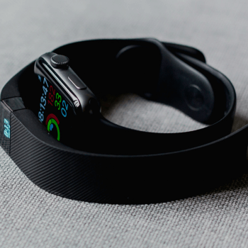 A black fitness tracker with a display showing heart rate and time, resting on a textured gray surface.