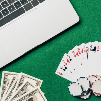 A laptop. playing cards, poker chips and cash on a table