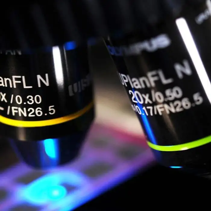 A close-up of microscope lenses with a slide illuminated by blue light.