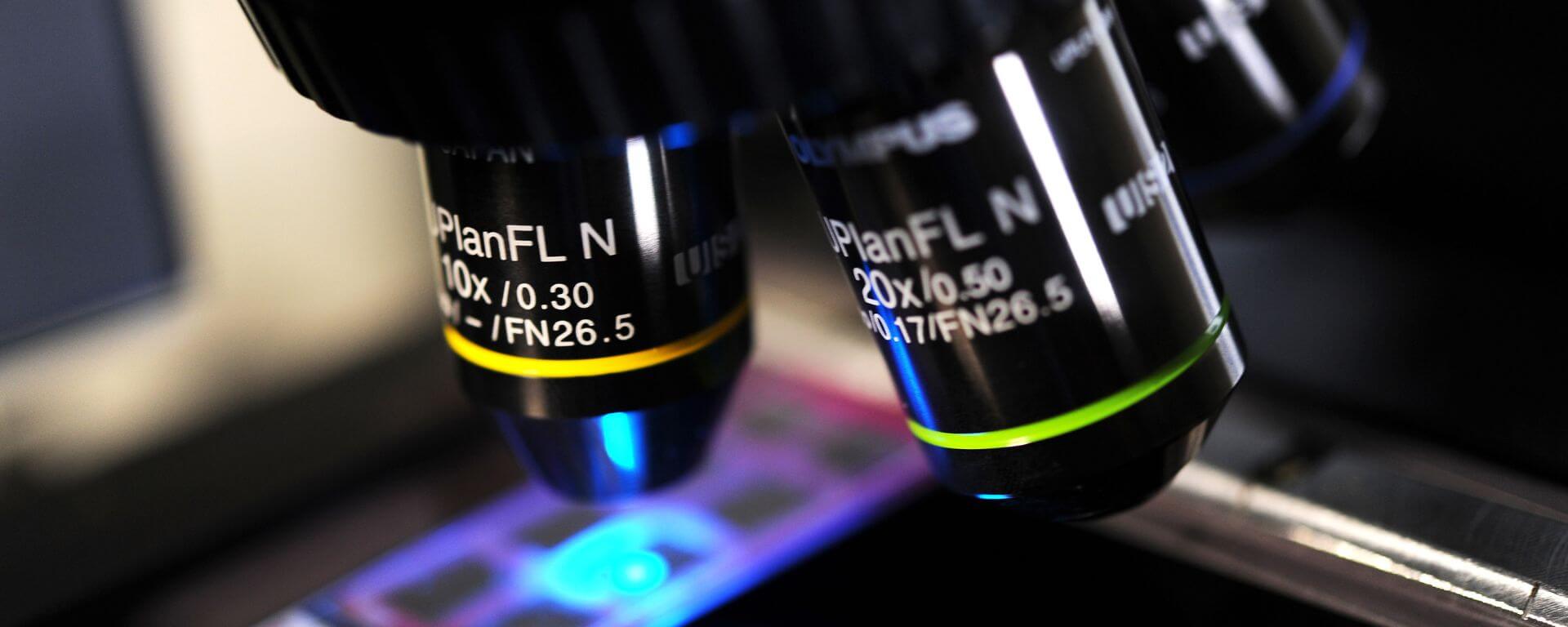 A close-up of microscope lenses with a slide illuminated by blue light.