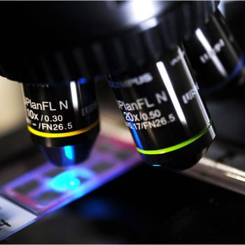 Close-up of microscope objectives with a blue light shining through one lens.